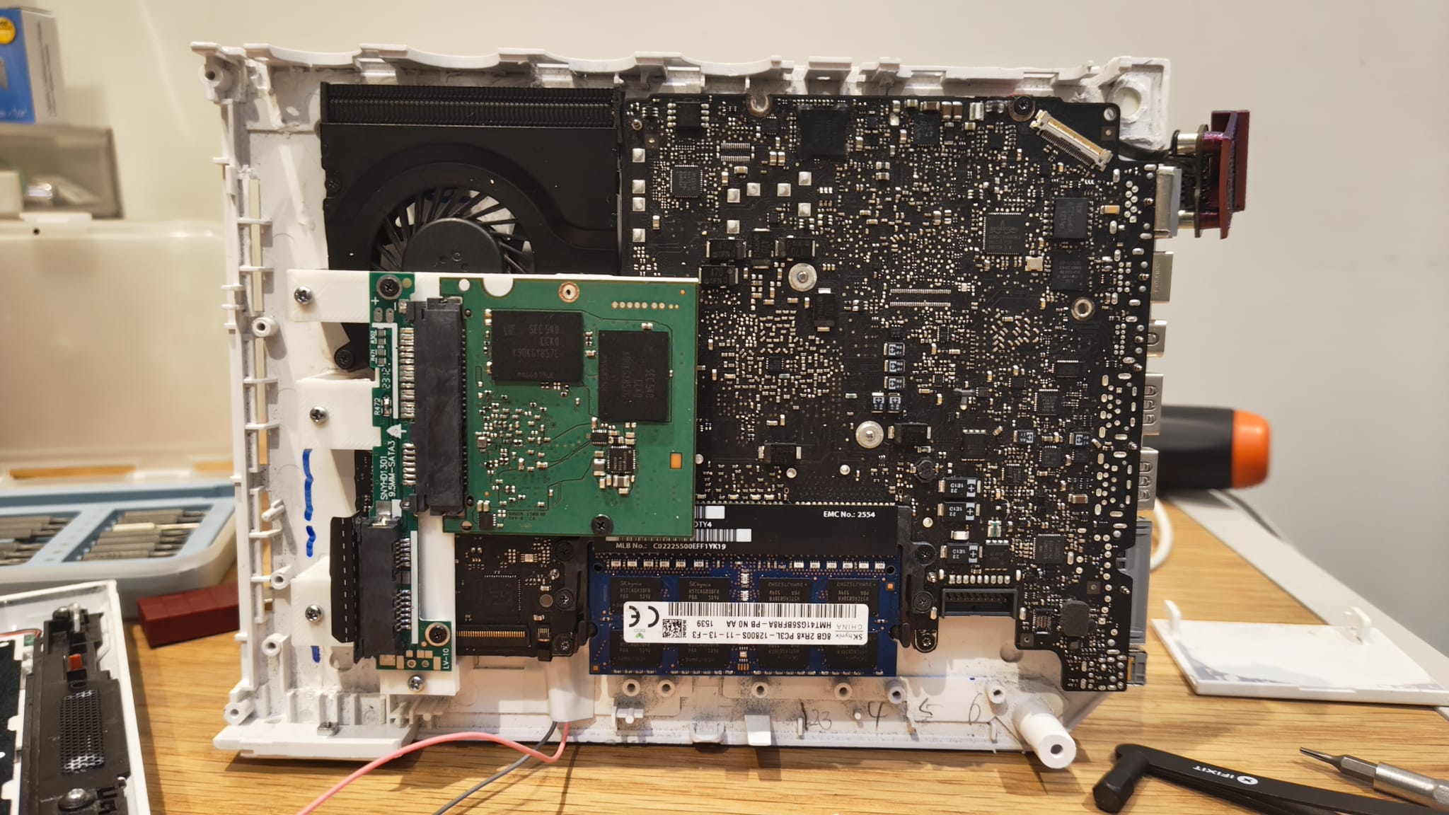 A photo of the bottom half of a Wii shell, with a black laptop motherboard and green SSD PCB attached.